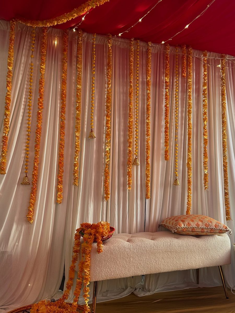 Budget mehndi decoration with marigold garlands and gold bells over a cream bridal bench — Petals and Bliss Toronto