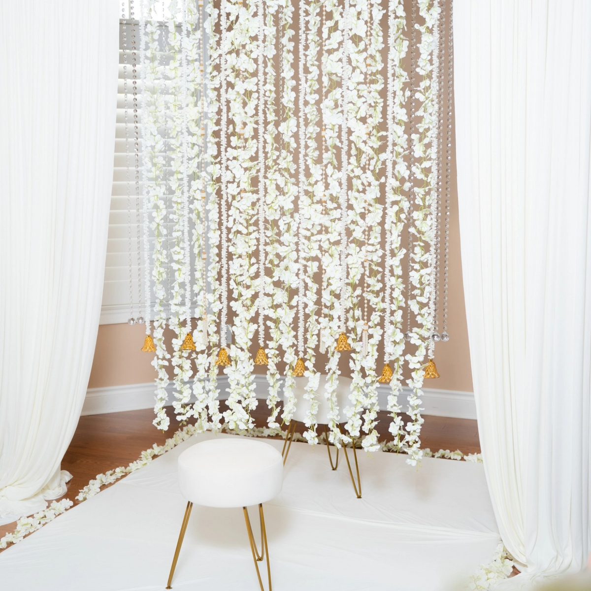 The Blossom package — white floral strands and gold bells framing a petal-edged seating corner, Indian wedding decor rental GTA